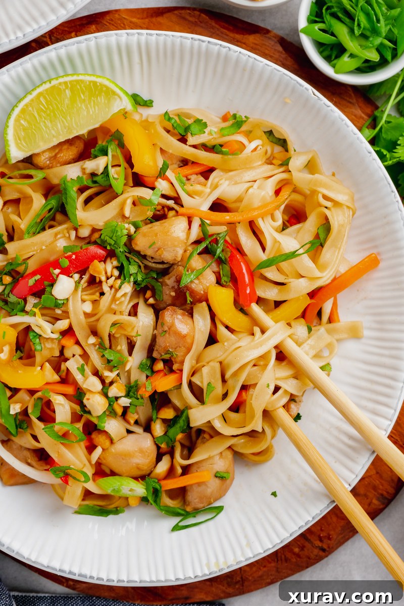 A white plate with Instant Pot Pad Thai, garnished with chopsticks, a lime wedge, chopped peanuts, and cilantro