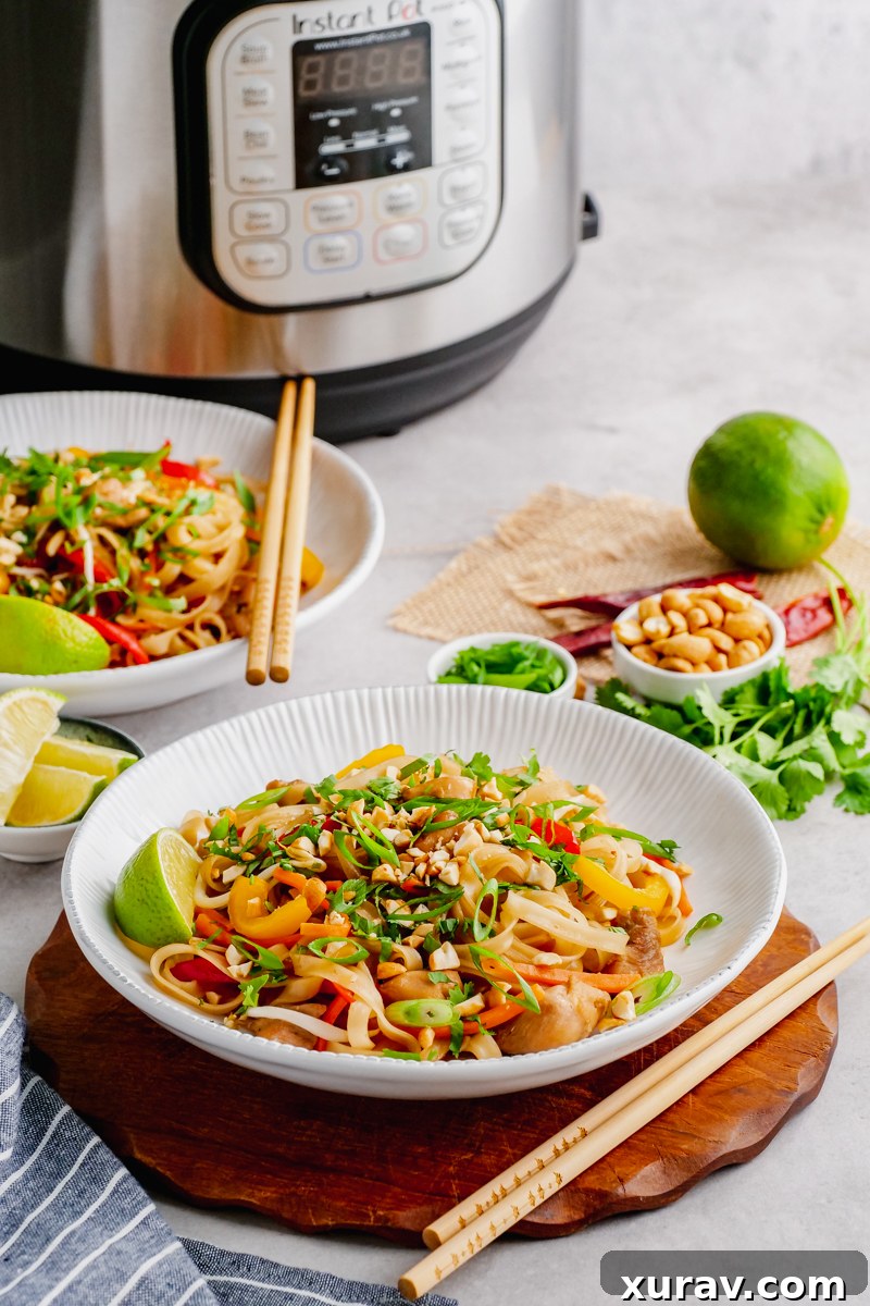 An Instant Pot in the background with bowls of Pad Thai, chopsticks, and fresh garnishes like lime and peanuts