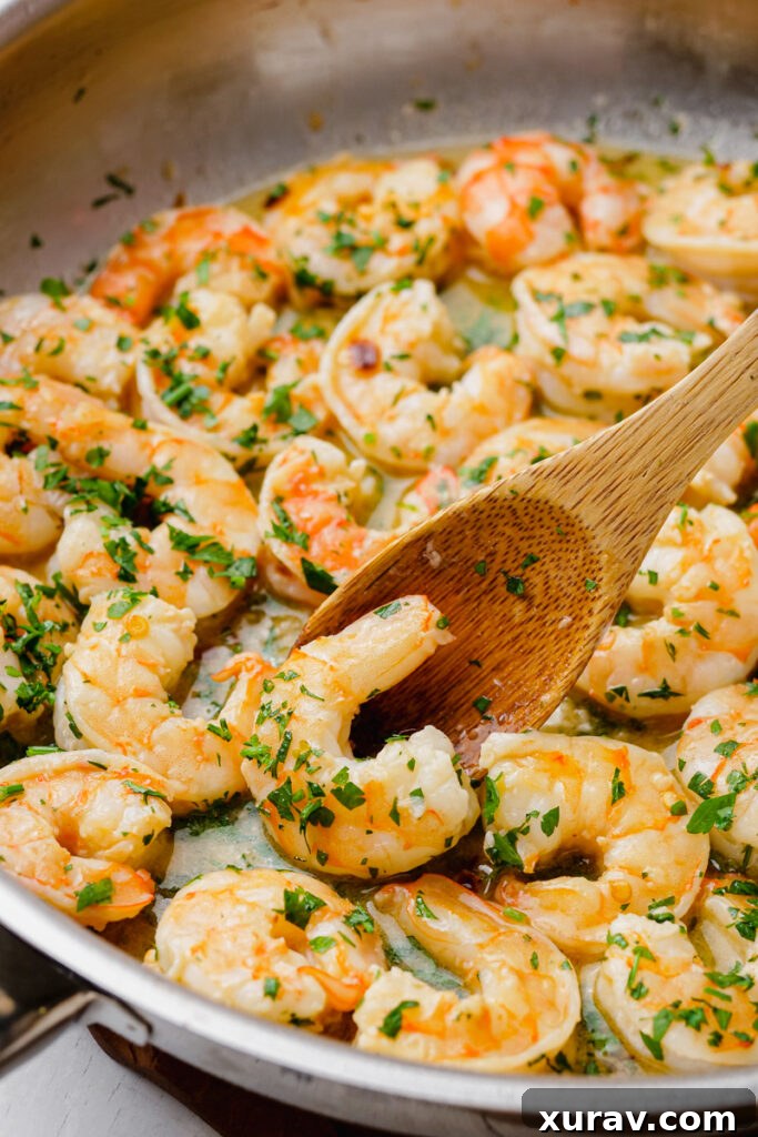 Shrimp scampi being gently transferred into a pot of linguine with a wooden spoon.