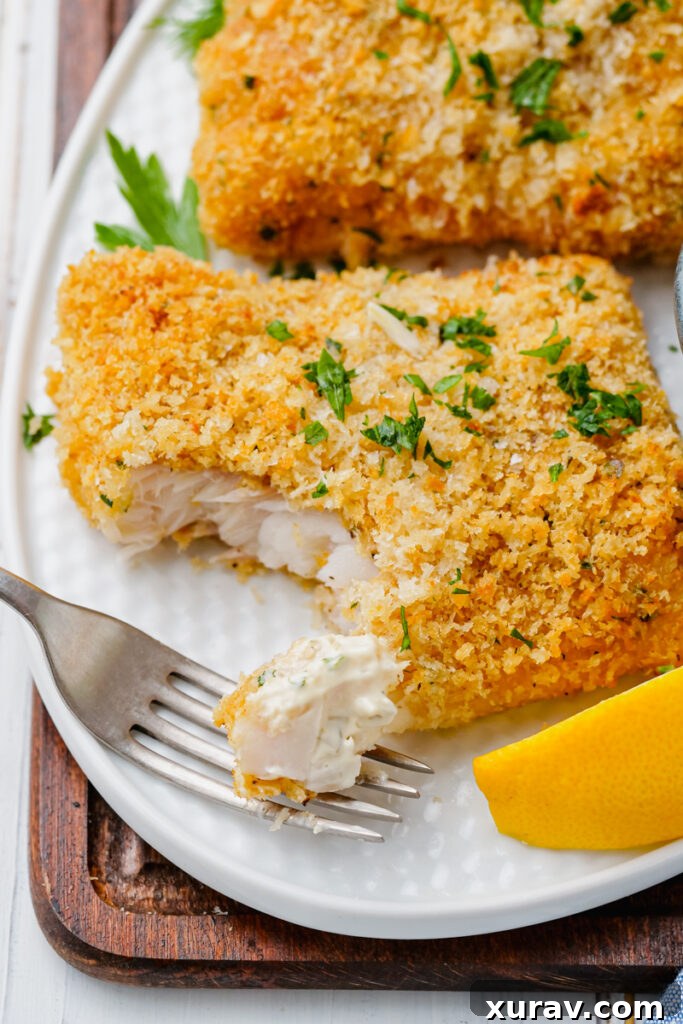 Oven fried fish on a white plate with flakes of it on a fork and lemon wedges