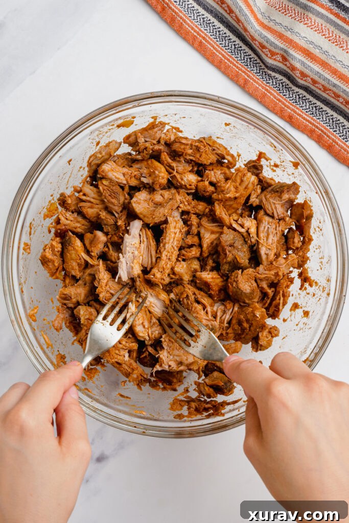 Shredding pork for pork mole tacos using two forks in a bowl.