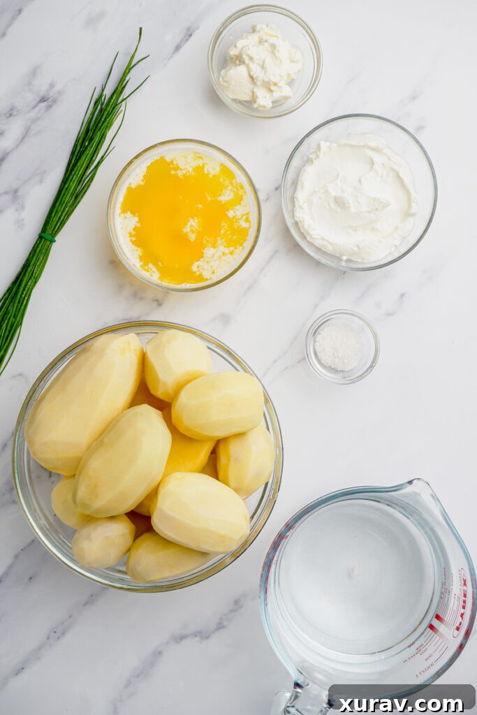 Ingredients laid out for slow cooker mashed potatoes, including russet potatoes, butter, sour cream, cream cheese, and fresh chives.