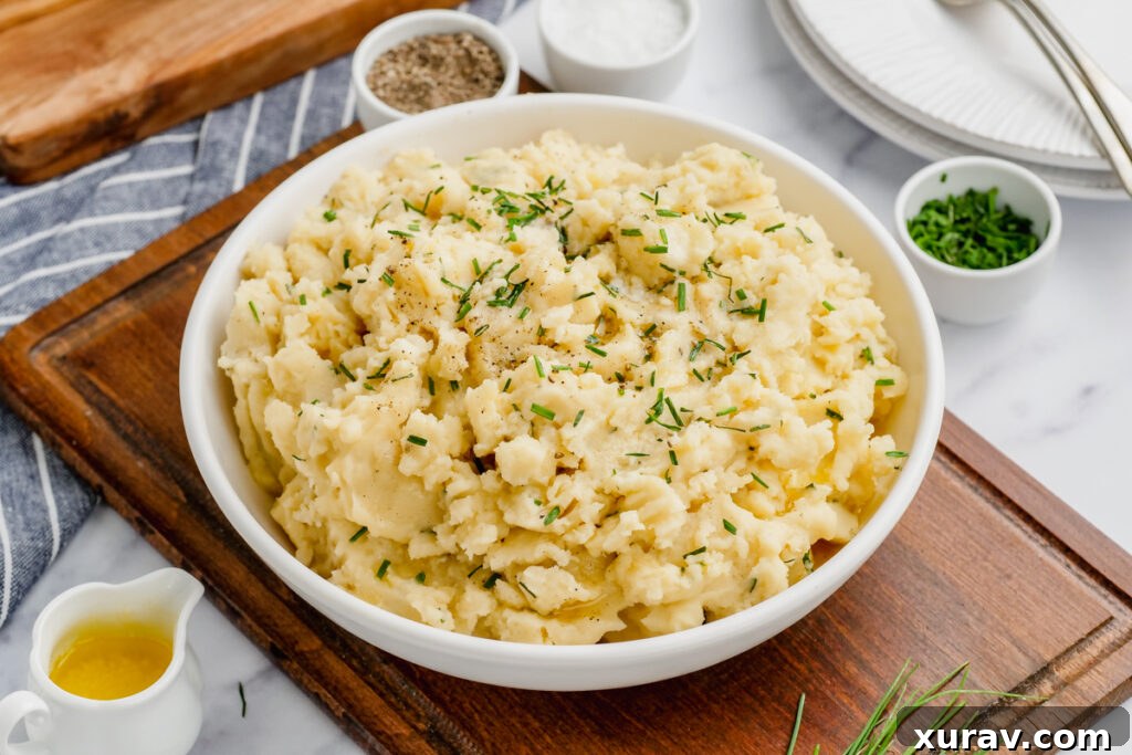 A beautifully presented white bowl of slow cooker mashed potatoes, garnished with fresh herbs and a pat of butter, ready to serve.