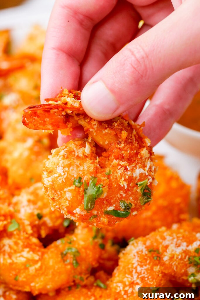 A hand holding a crispy oven baked shrimp, tail on