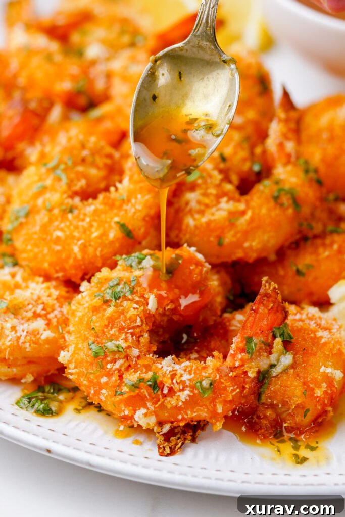 breaded shrimp that is oven baked on a white plate with sauce being spooned over the top. 