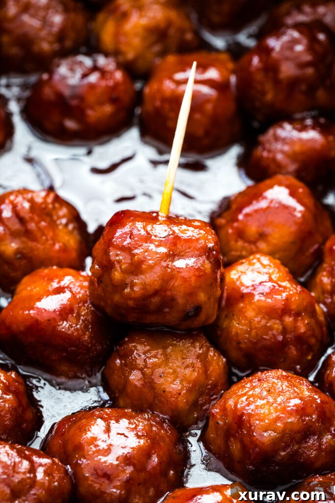 Sticky Sweet Slow Cooker Meatballs 2 A close-up of delicious crockpot grape jelly meatballs on a white platter, garnished with fresh parsley.