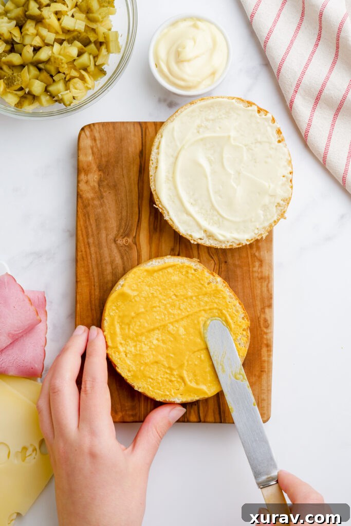 The bottom half of a potato roll spread with yellow mustard, ready for layering.