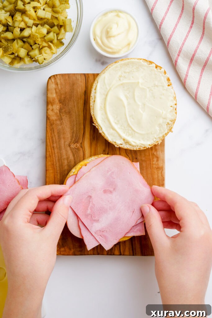 Thinly sliced ham and roast pork layered on the mustard-covered bottom bun of a Cuban sandwich.