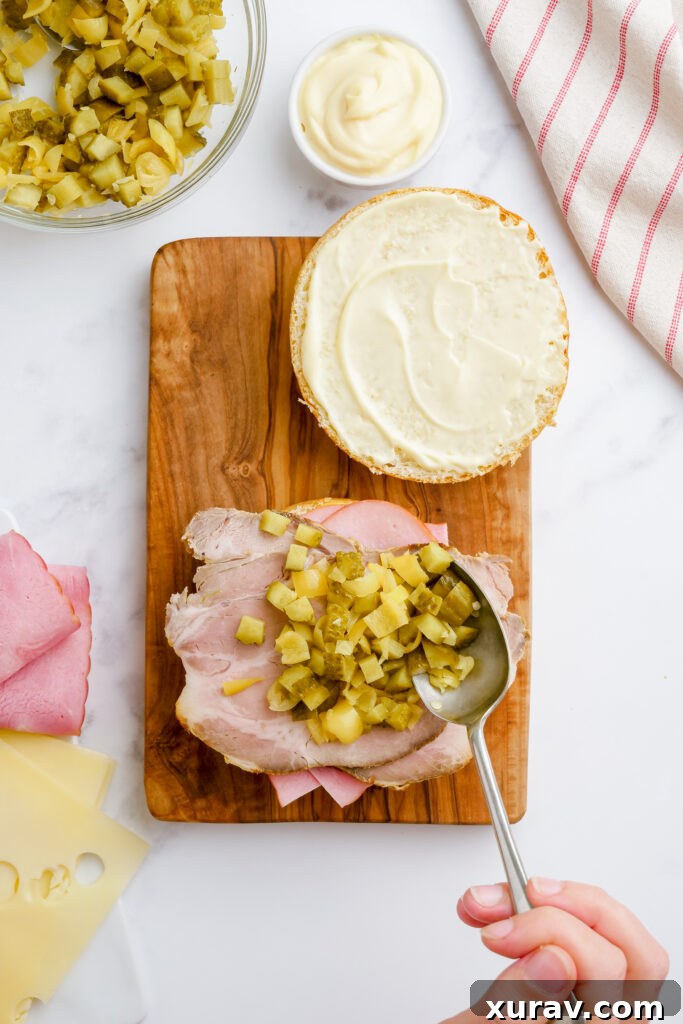 Diced pickles and banana peppers, topped with Swiss cheese slices, layered on the meats of a Cuban sandwich.