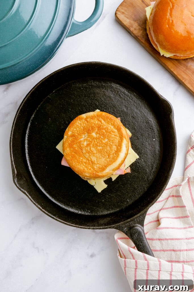 A Cuban sandwich being pressed between two heavy cast iron skillets on a stovetop.