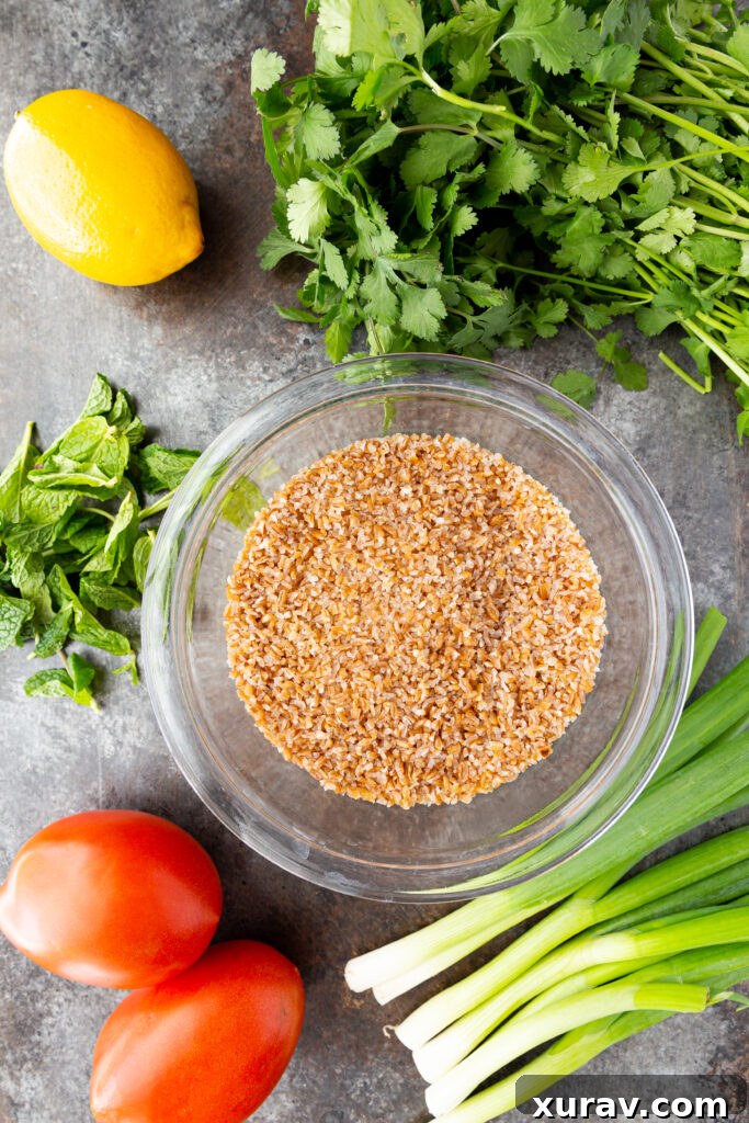 A flat lay photograph displaying all the fresh ingredients needed to make Tabbouleh: fresh parsley, mint, ripe tomatoes, green onions, bulgur, lemons, olive oil, and a bowl of bright red pomegranate arils.
