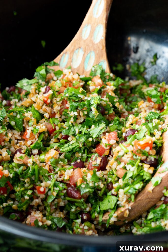A close-up shot of the finished Tabbouleh salad in a bowl, highlighting the vibrant green herbs, red tomatoes, and glistening pomegranate arils, perfectly dressed and ready to serve.