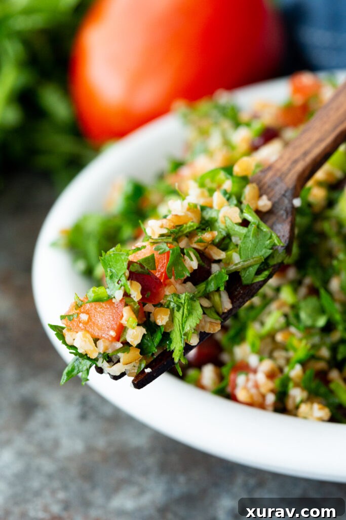 A forkful of Tabbouleh, showcasing the finely chopped herbs, bulgur, and pomegranate arils, ready to be eaten.