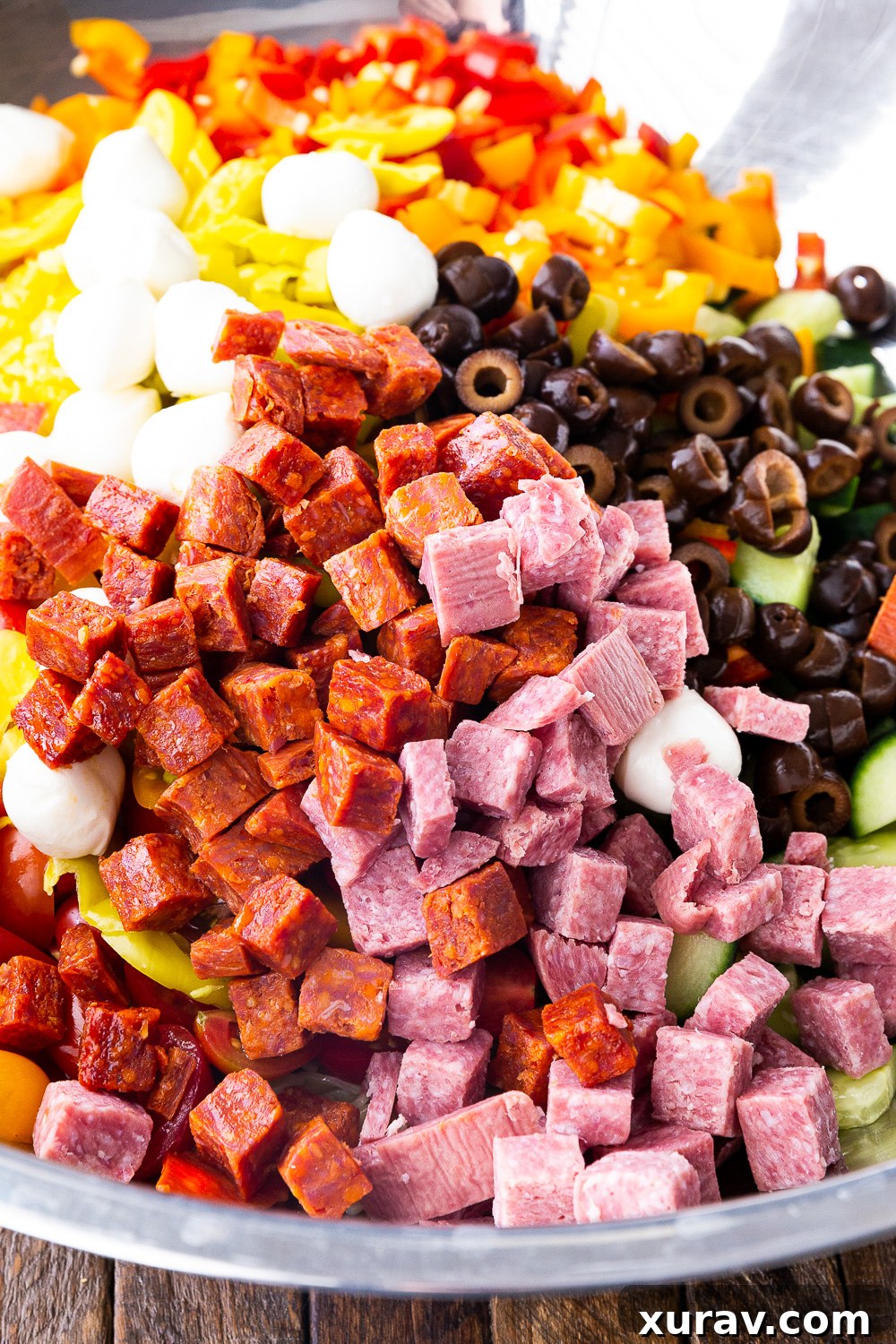 All the vibrant ingredients for the pasta salad being gently mixed in a large bowl, ensuring even distribution of flavors.