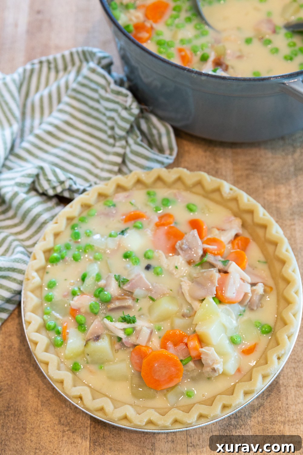 Pouring filling into the pie crust for chicken pot pie. 