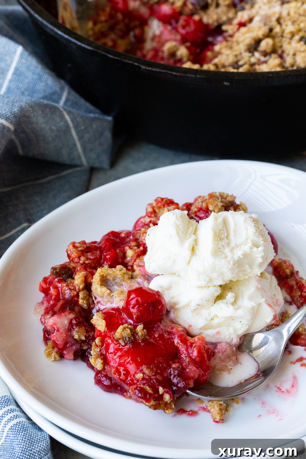 A delicious cherry cobbler, with oatmeal crumble on top and vanilla ice cream, perfectly plated in a serving dish.