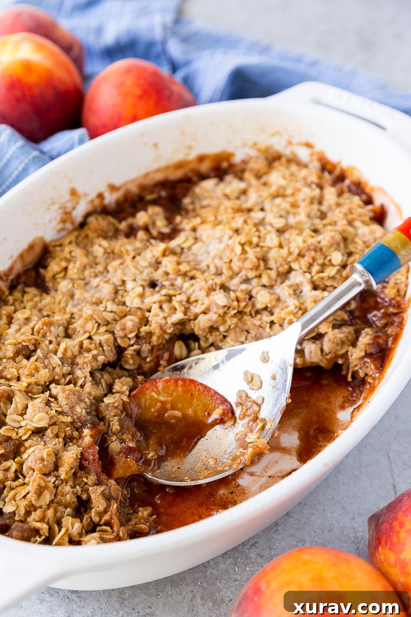 Warm, gooey peach crisp with a golden oat topping and a spoonful missing—revealing the sweet, bubbling peach filling underneath.
