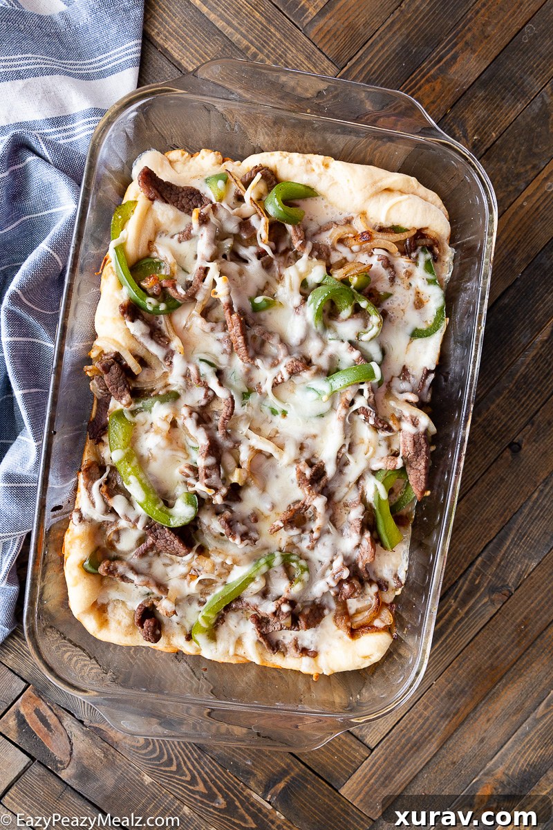 A glorious slice of Philly Cheesesteak Bake, showing the layers of dough, queso blanco, steak, peppers, onions, and melted provolone.