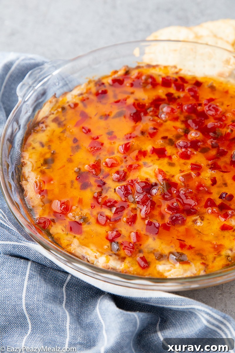 A close-up of the finished Bacon Pepper Jelly Dip, showing the gooey cheese, crispy bacon, and glossy pepper jelly, ready to be scooped.