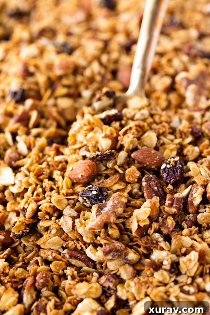 A close-up of the homemade granola mix spread evenly on a baking sheet, with a wooden spoon scooping it, ready for the oven.